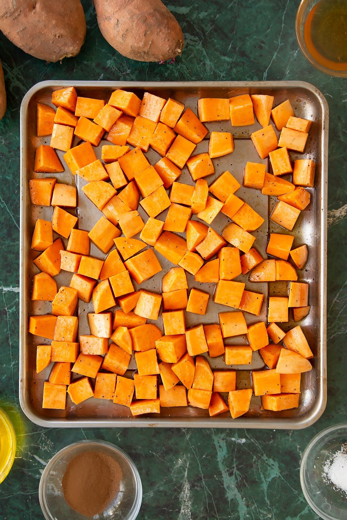 The sheet pan of sliced sweet potatoes having been mixed together with the oil, honey and spices. 