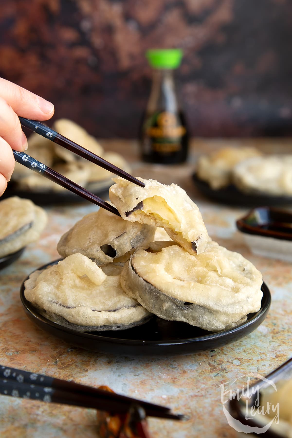 Chopsticks reaching in to grab a peice of eggplant tempura.