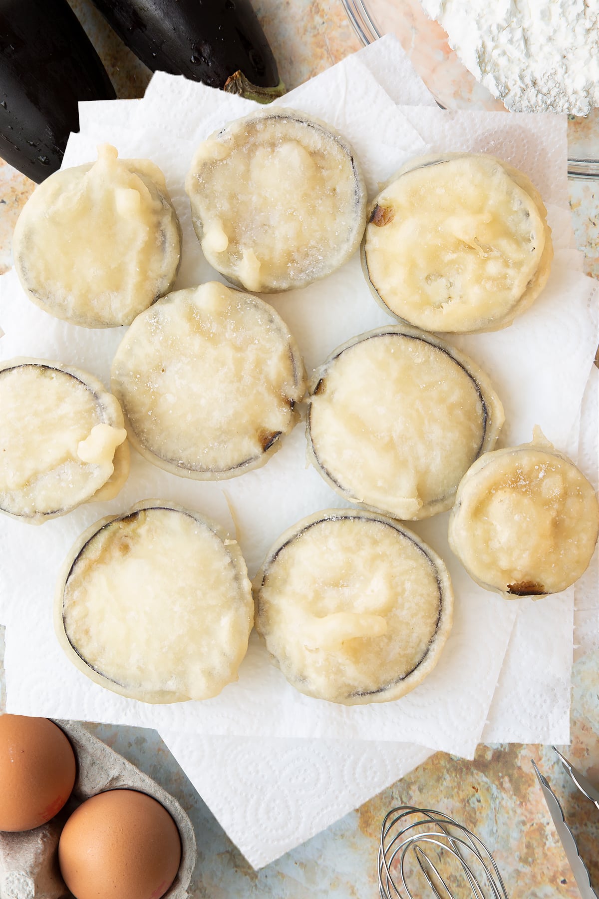 Eggplant slices covered in batter on slices of kitchen paper.