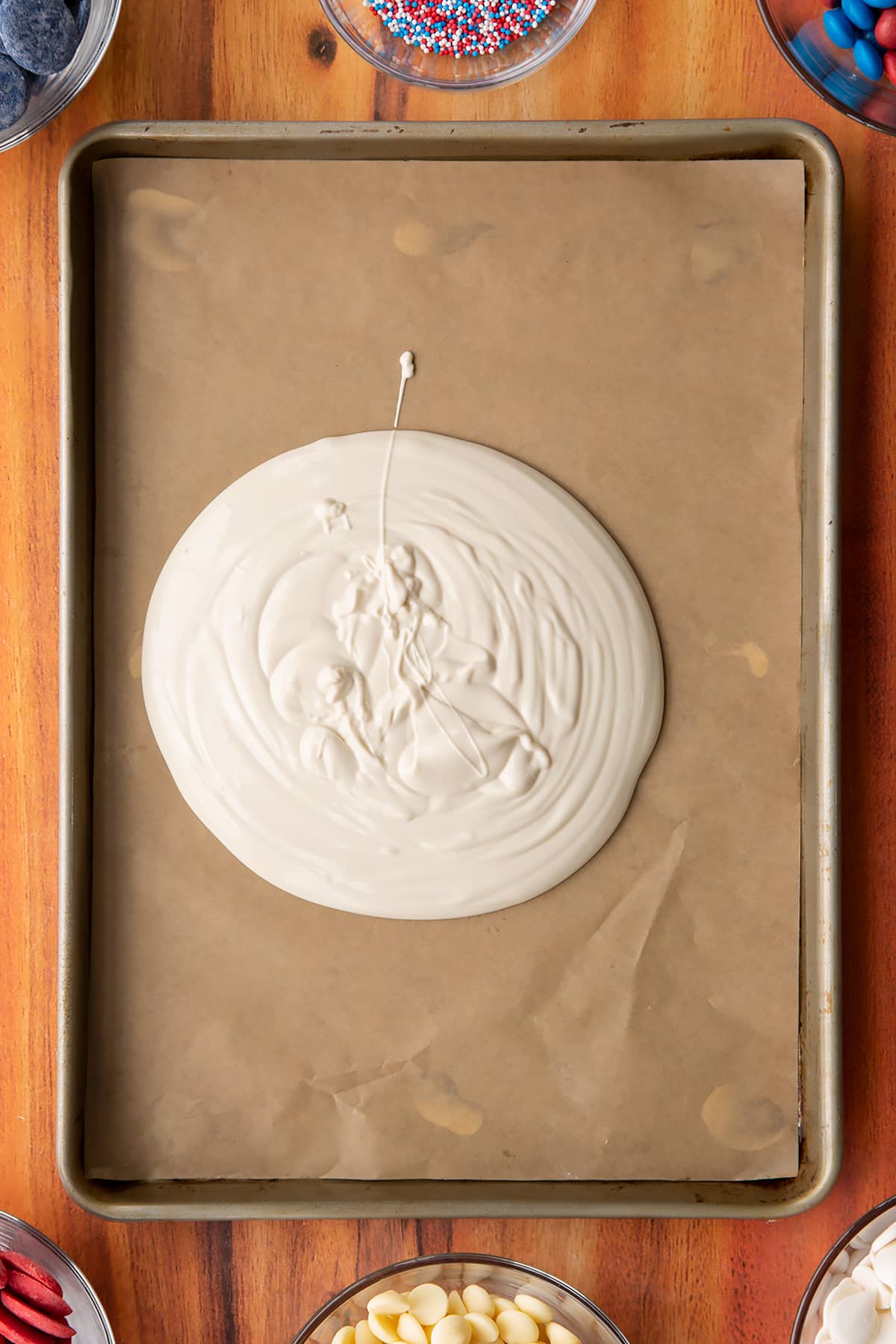 White candy being poured onto a sheetpan lined with baking paper.