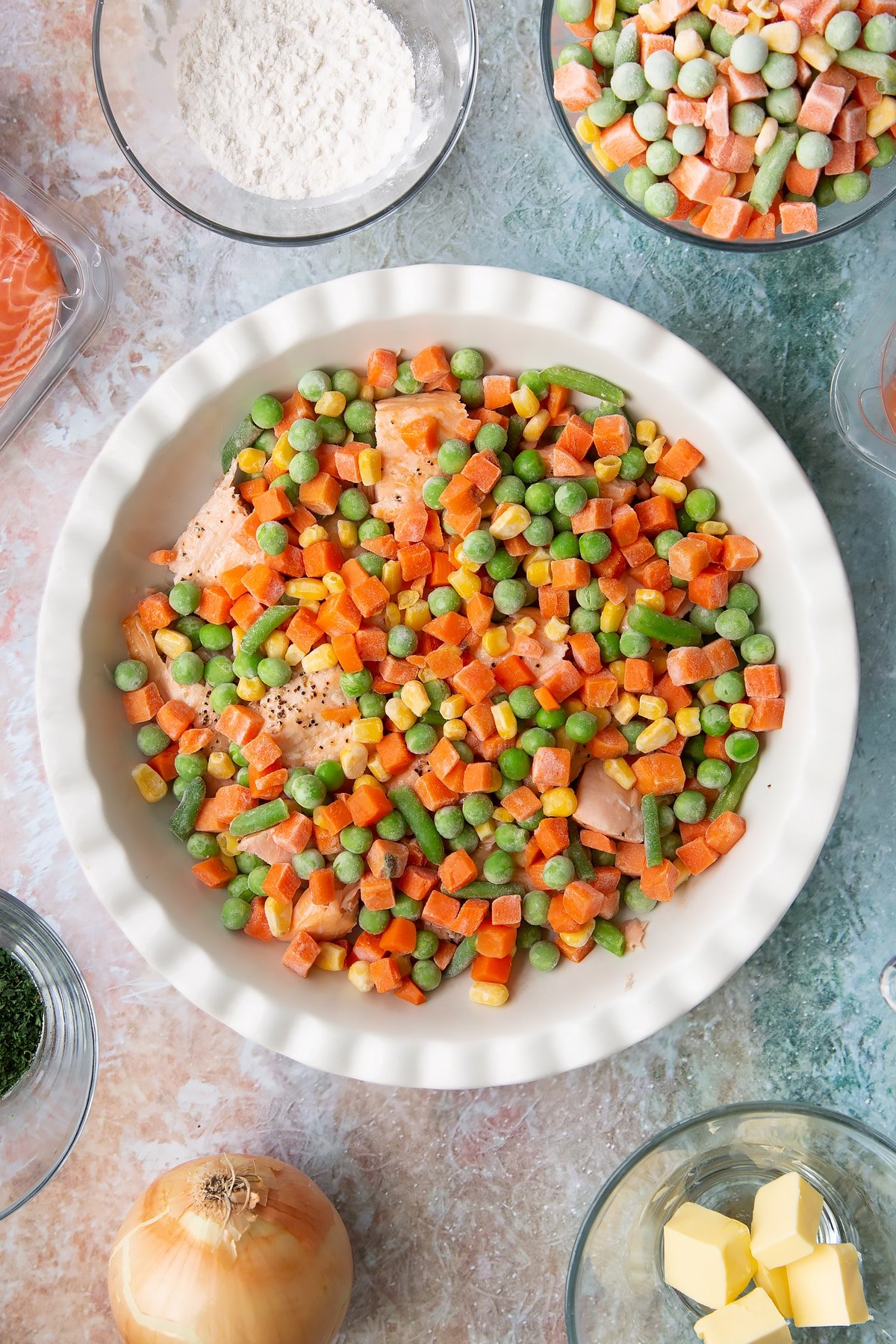 Overhead shot of the pan of salmon pieces having been covered in frozen peas and carrots.